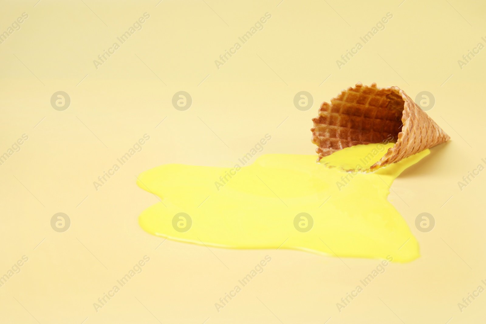 Photo of Melted ice cream and wafer cone on yellow background, space for text