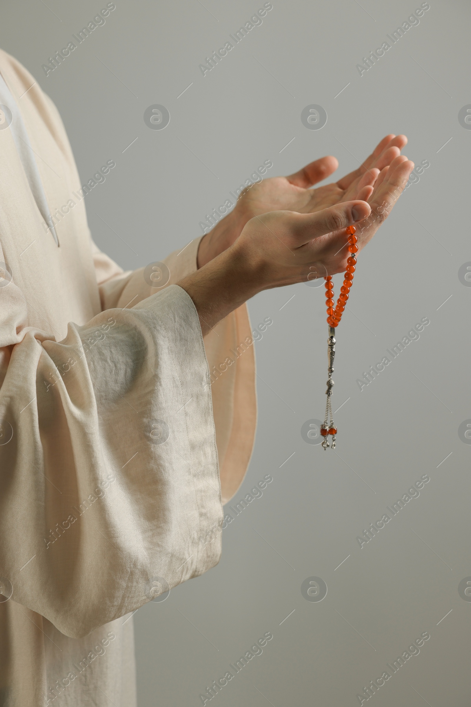 Photo of Muslim man with misbaha praying on light grey background, closeup