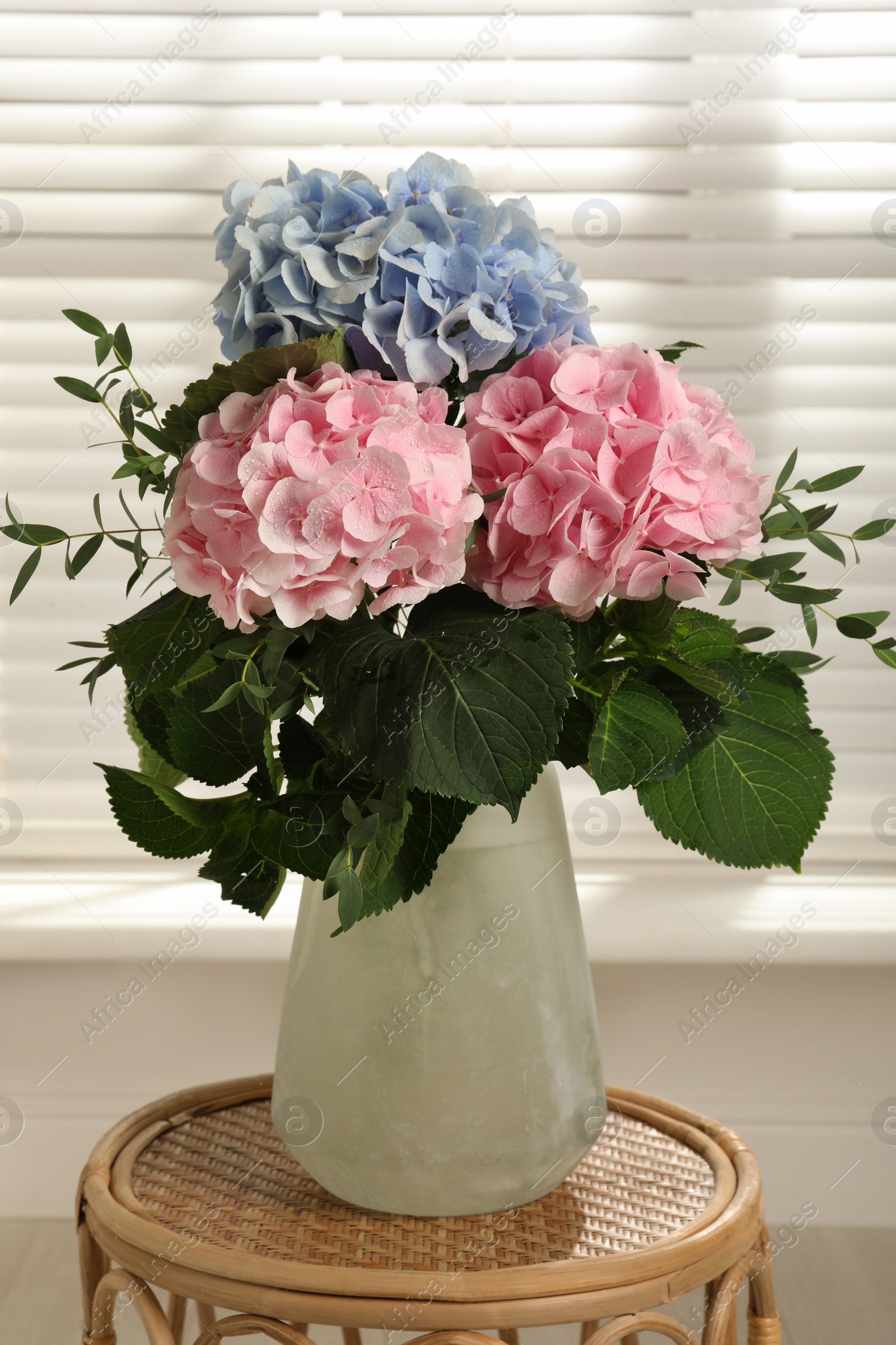 Photo of Beautiful hortensia flowers in vase on wicker stand indoors