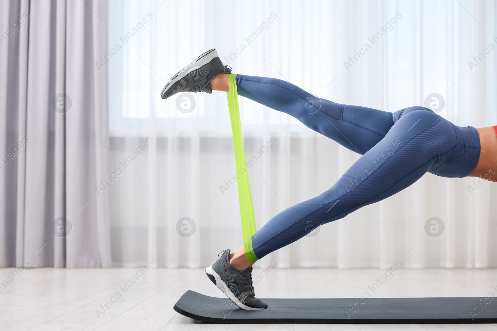 Photo of Woman doing exercise with fitness elastic band on mat indoors, closeup