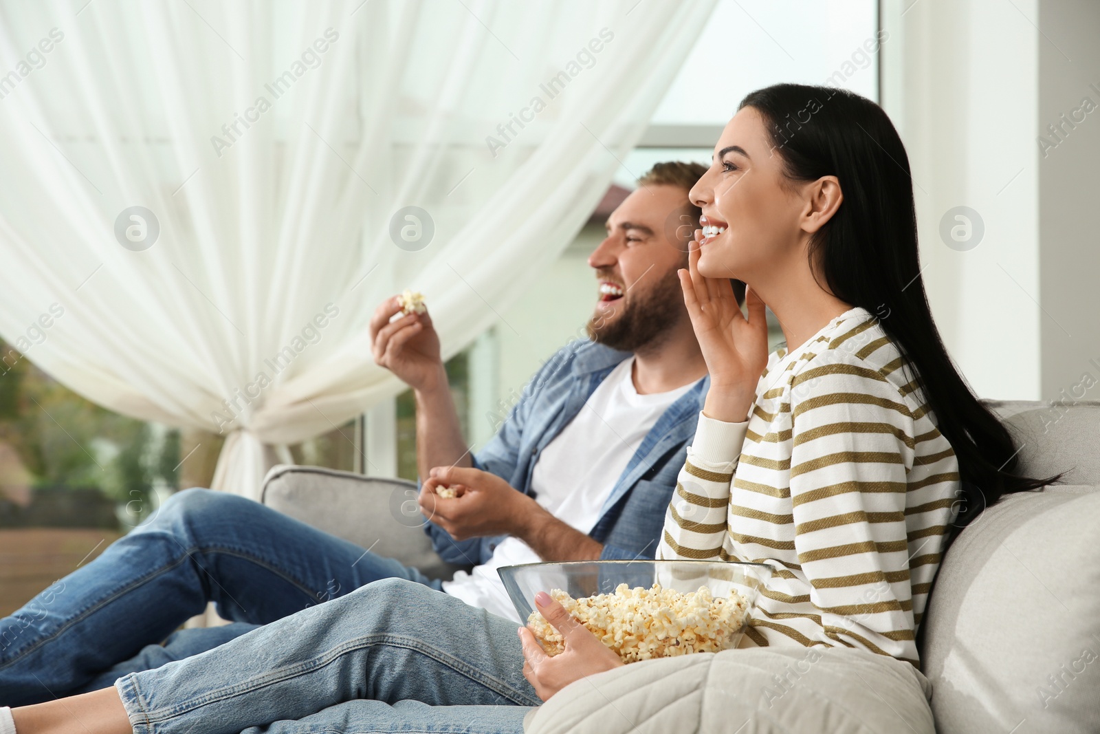 Photo of Happy couple watching movie with popcorn at home