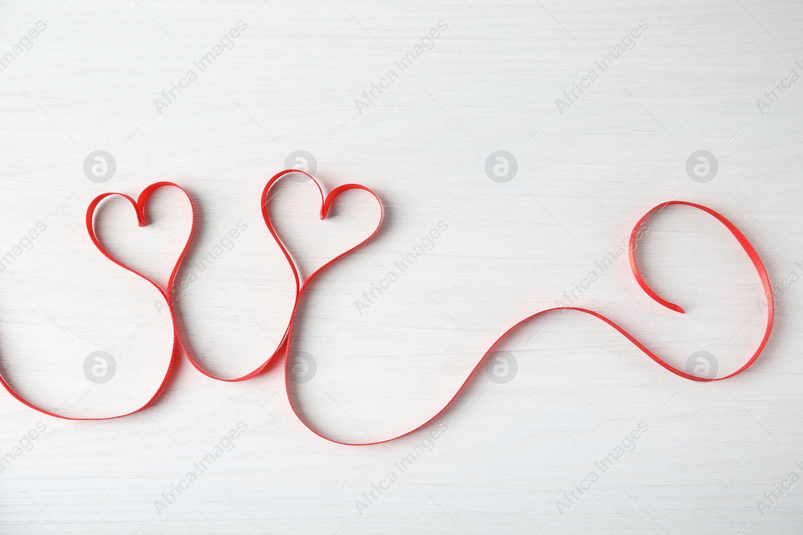 Photo of Hearts made of red ribbon on white wooden background, top view. Valentine's day celebration