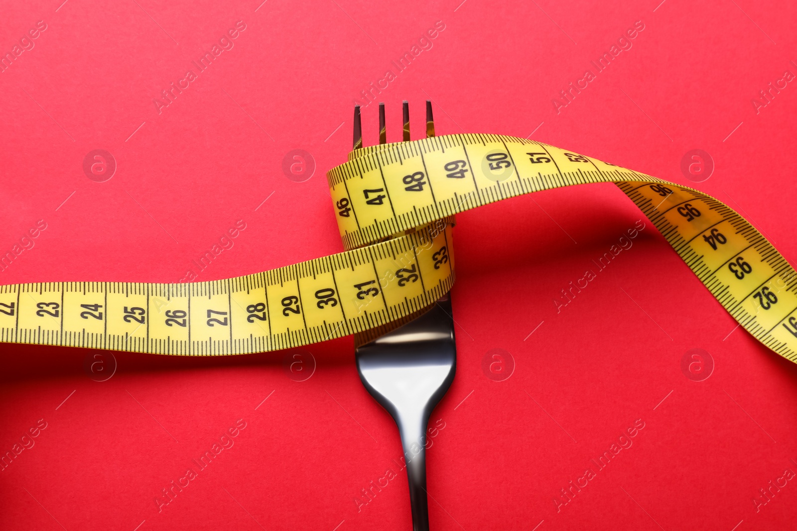 Photo of Fork with measuring tape on red background, top view. Diet concept