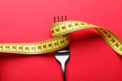 Fork with measuring tape on red background, top view. Diet concept