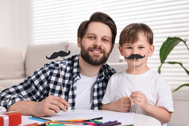 Photo of Happy dad and son with paper mustaches at home