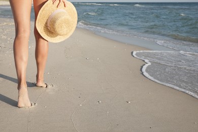 Photo of Woman with straw hat walking on beach near sea, closeup
