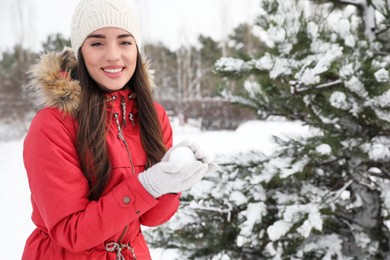Photo of Happy young woman with snowball outdoors on winter day. Space for text