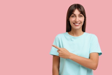 Photo of Special promotion. Happy woman pointing at something on pink background, space for text