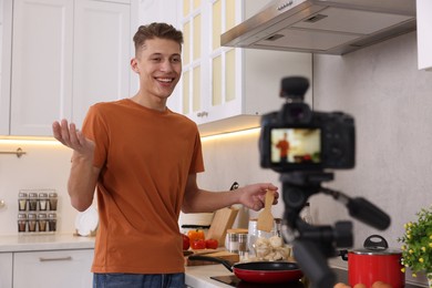 Photo of Smiling food blogger explaining something while recording video in kitchen