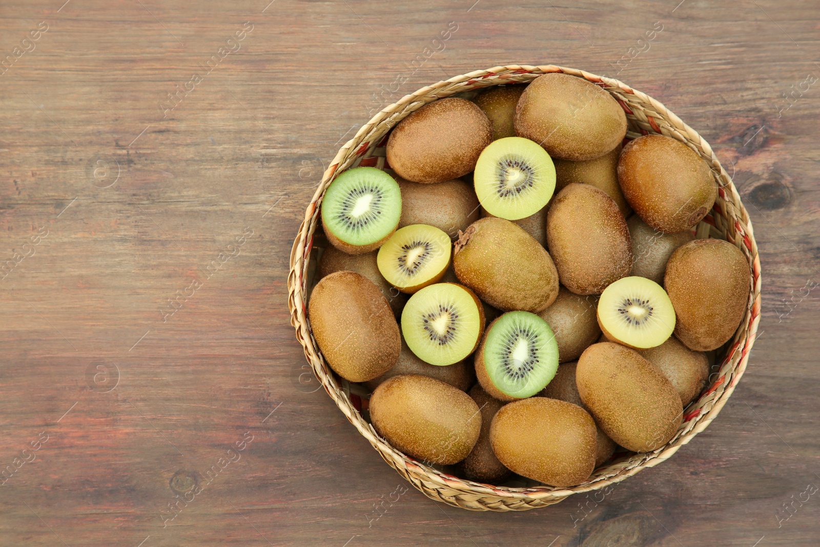 Photo of Basket of many whole and cut fresh kiwis on wooden table, top view. Space for text