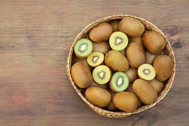 Photo of Basket of many whole and cut fresh kiwis on wooden table, top view. Space for text