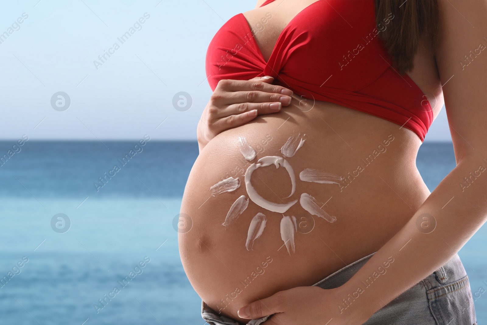 Image of Young pregnant woman with sun protection cream on beach, closeup