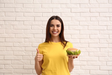 Young woman with tasty burger near brick wall