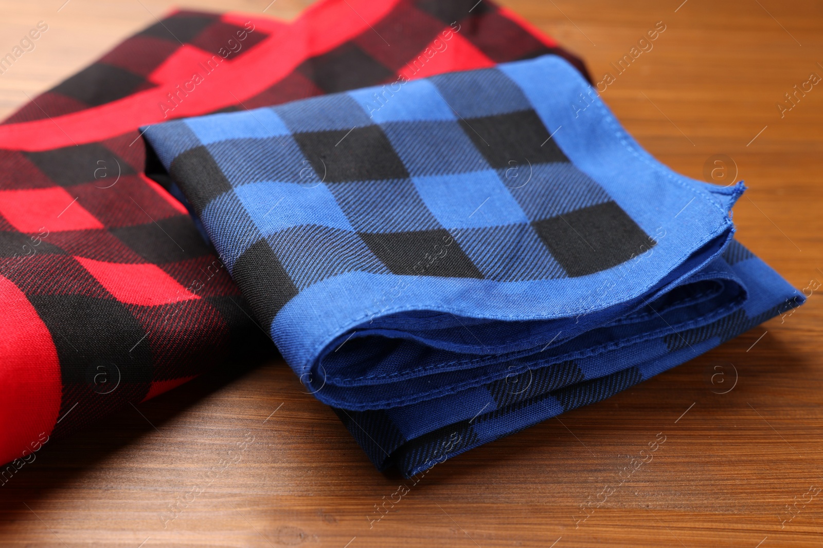 Photo of Folded red and blue checkered bandanas on wooden table, closeup