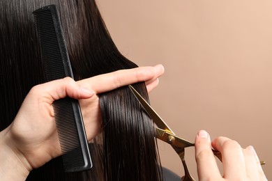 Hairdresser cutting client's hair with scissors on light brown background, closeup. Space for text