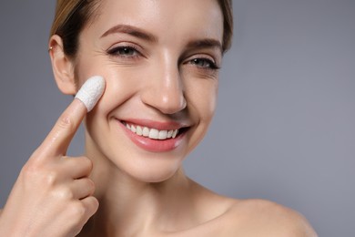 Photo of Woman using silkworm cocoon in skin care routine on grey background, closeup. Space for text