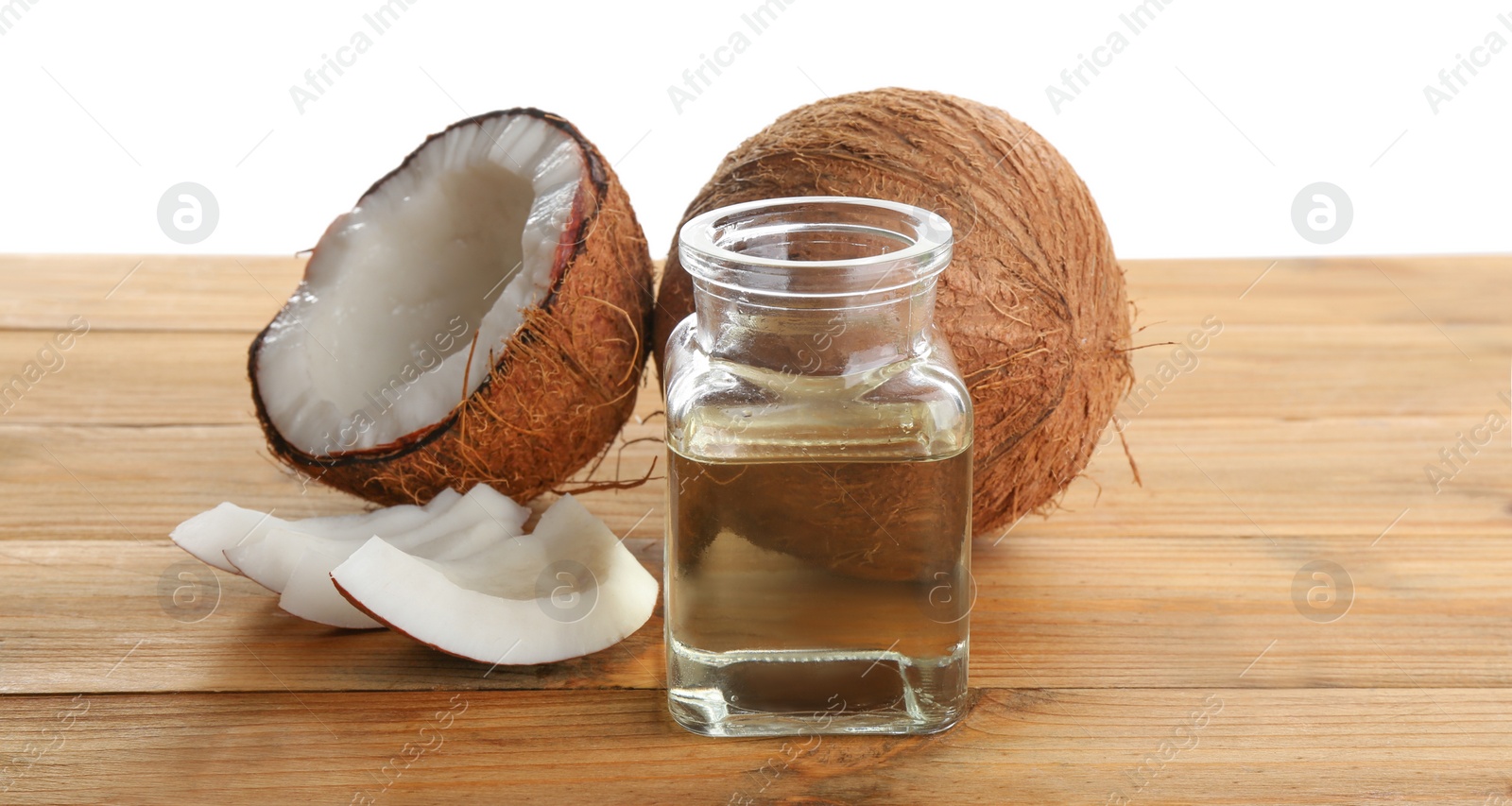 Photo of Ripe coconuts and jar with natural organic oil on wooden table against white background