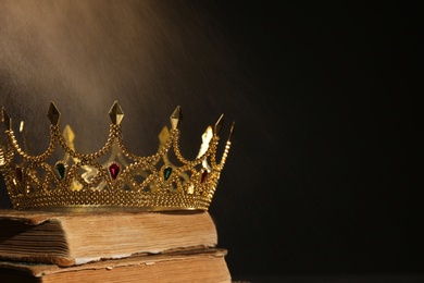 Photo of Beautiful golden crown and old books on black background, space for text. Fantasy item