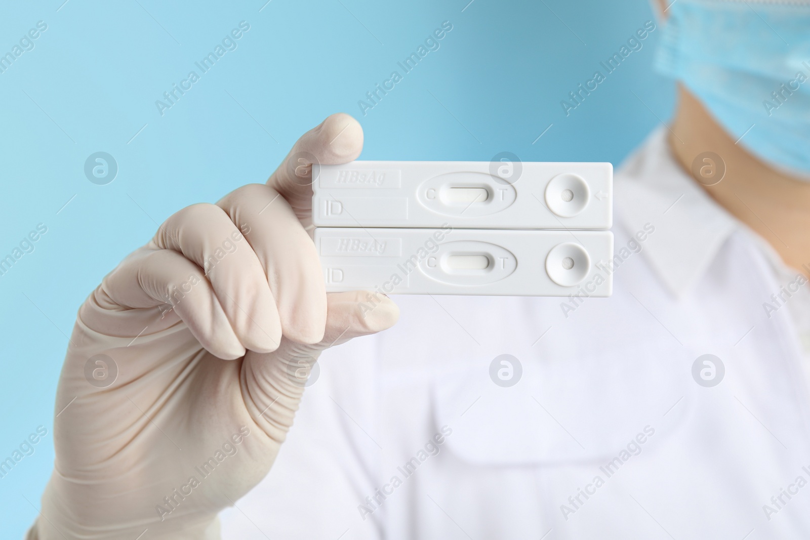 Photo of Doctor holding two disposable express tests for hepatitis on light blue background, closeup