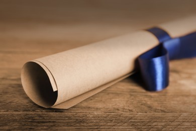 Image of Rolled student's diploma with blue ribbon on wooden table, closeup