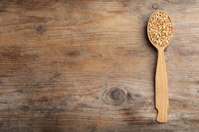 Photo of Spoon with green buckwheat on wooden table, top view. Space for text