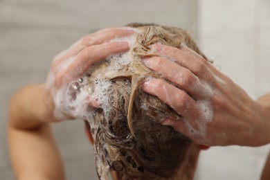 Woman washing hair with shampoo indoors, closeup