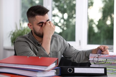 Overwhelmed man sitting at table with documents in office