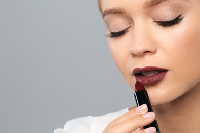 Photo of Beautiful woman applying dark lipstick on gray background. Space for text