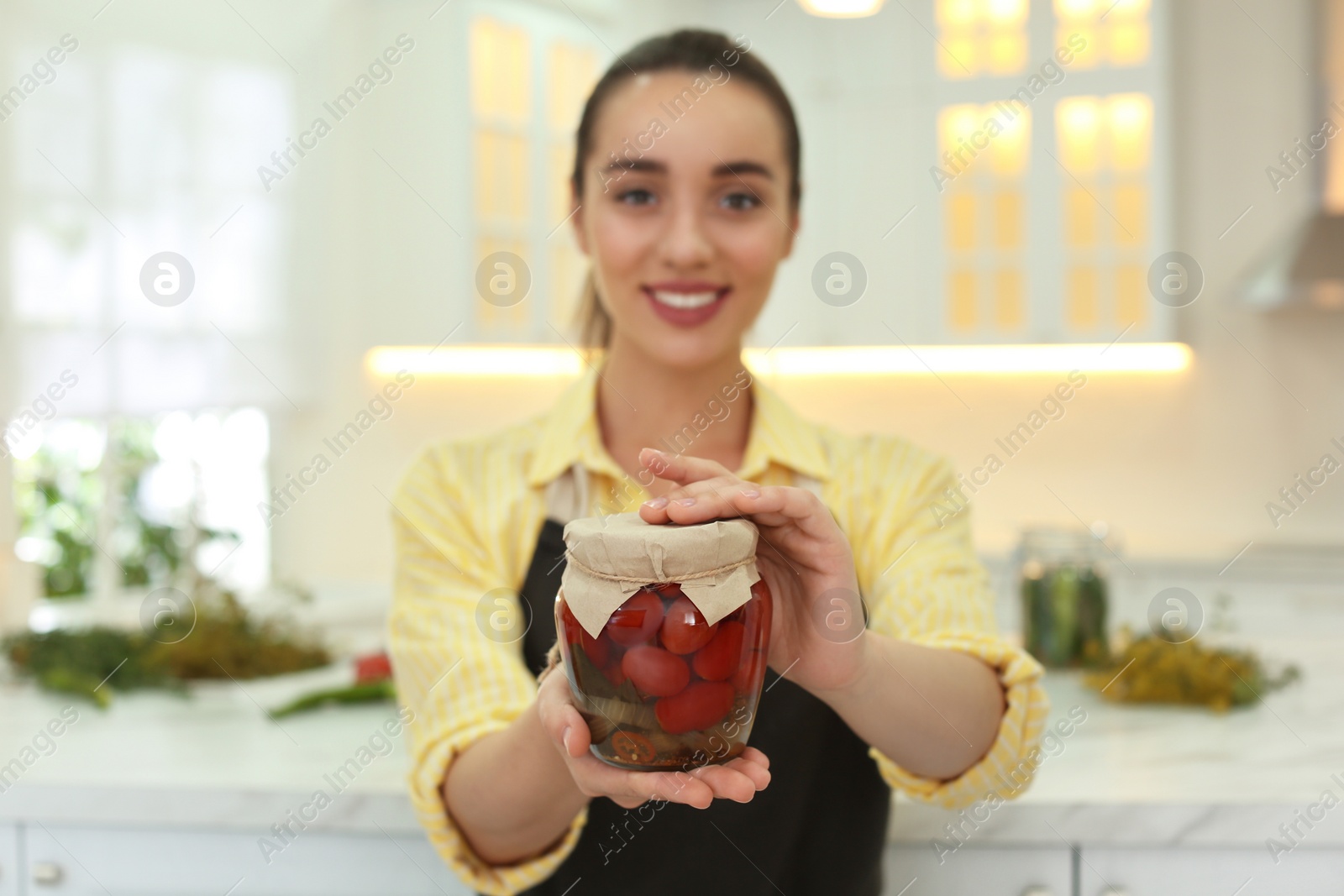 Photo of Woman holding jar of pickled vegetables in kitchen, focus on hands