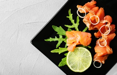 Photo of Plate with fresh sliced salmon fillet, lemon and arugula on light background, top view