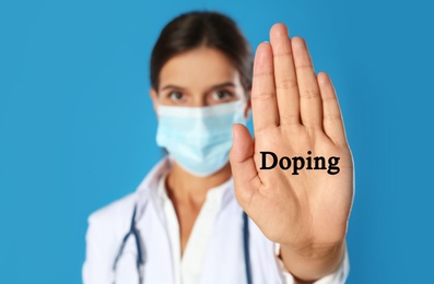 Image of Doctor in protective mask showing stop gesture against blue background, focus on hand. Doping control