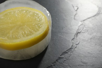 Photo of Piece of ice with lemon slice on black table, closeup. Space for text