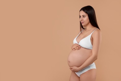Photo of Beautiful pregnant woman in stylish comfortable underwear on beige background, space for text