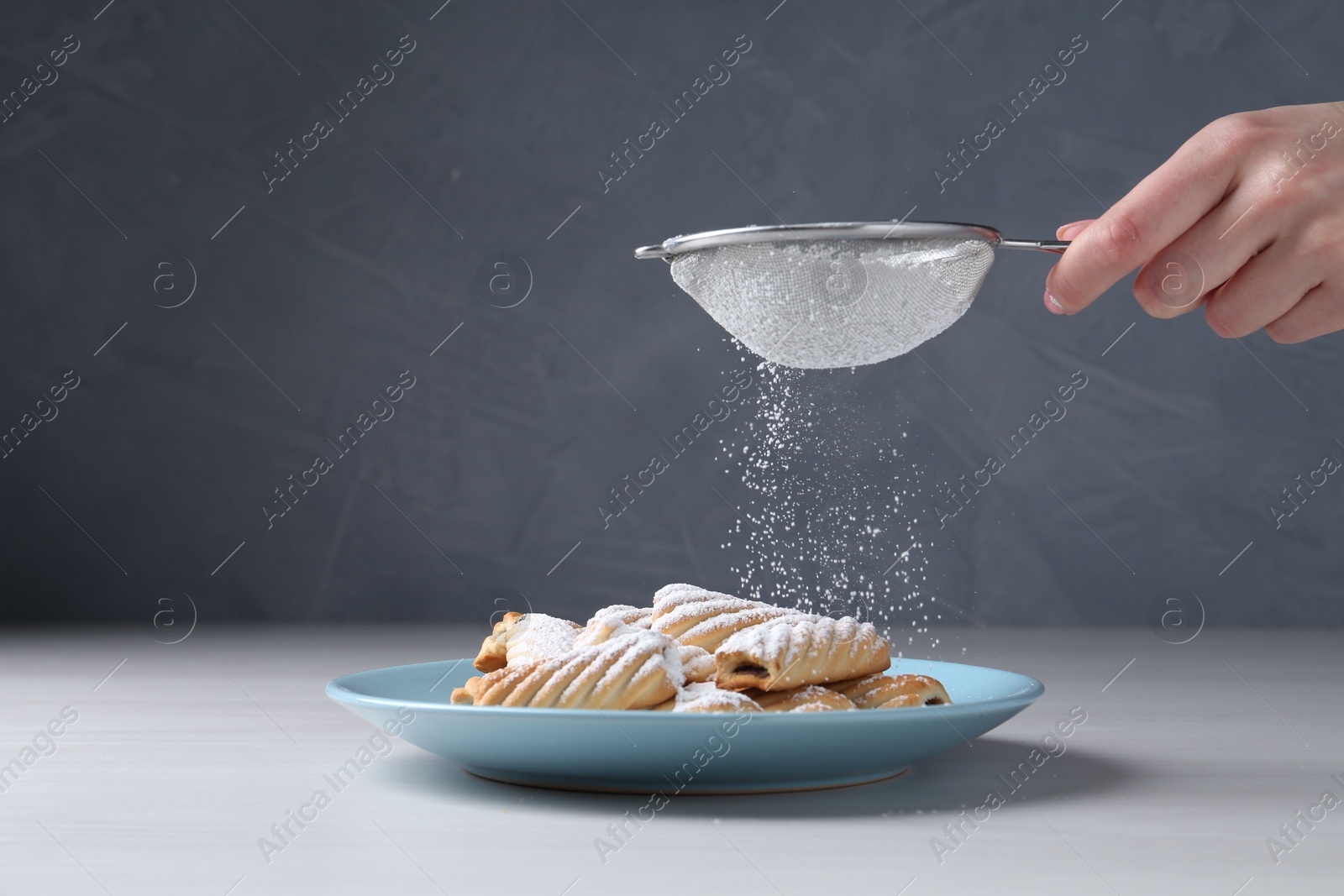 Photo of Woman with sieve sprinkling powdered sugar onto cookies at white wooden table, closeup