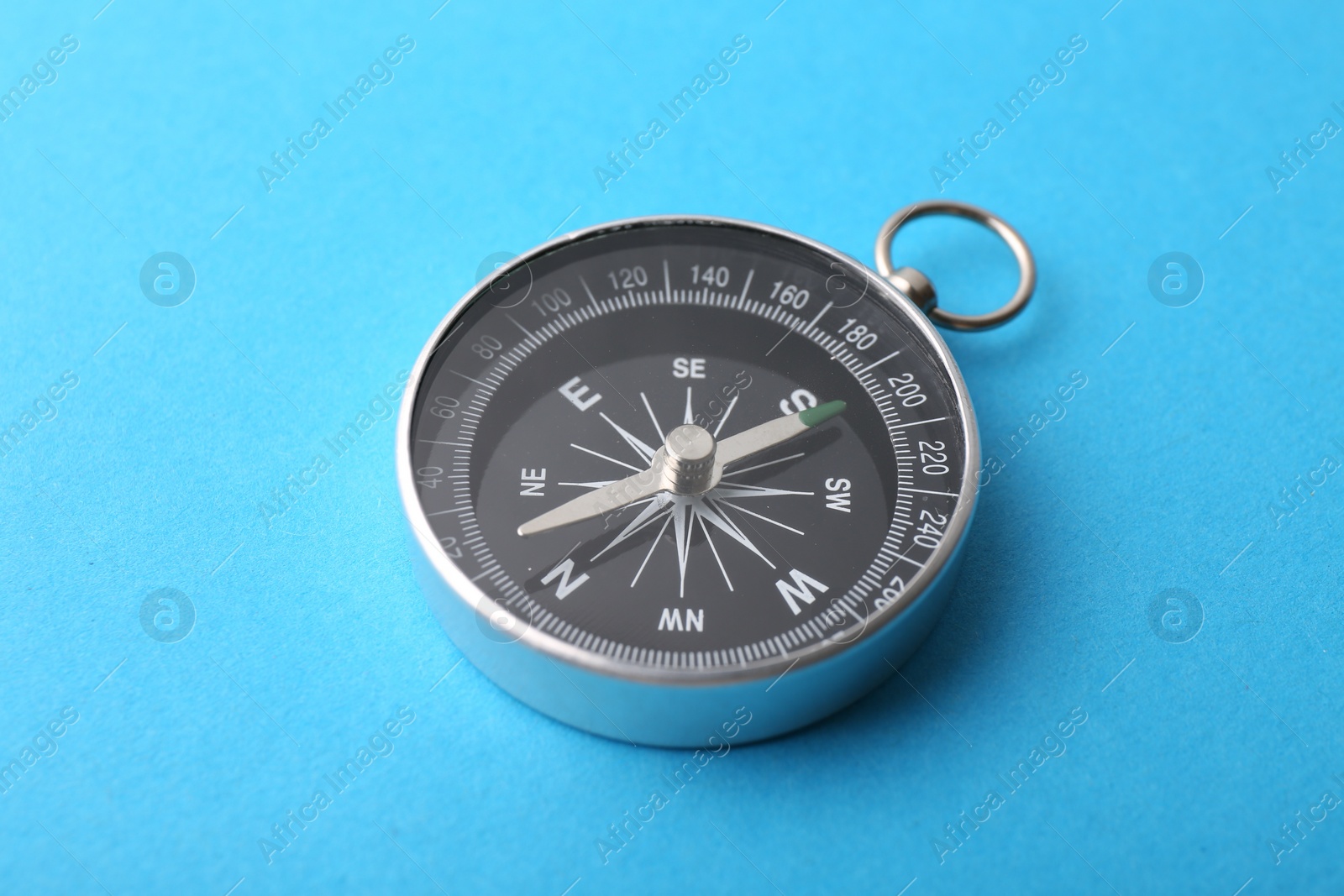 Photo of One compass on light blue background, closeup. Tourist equipment