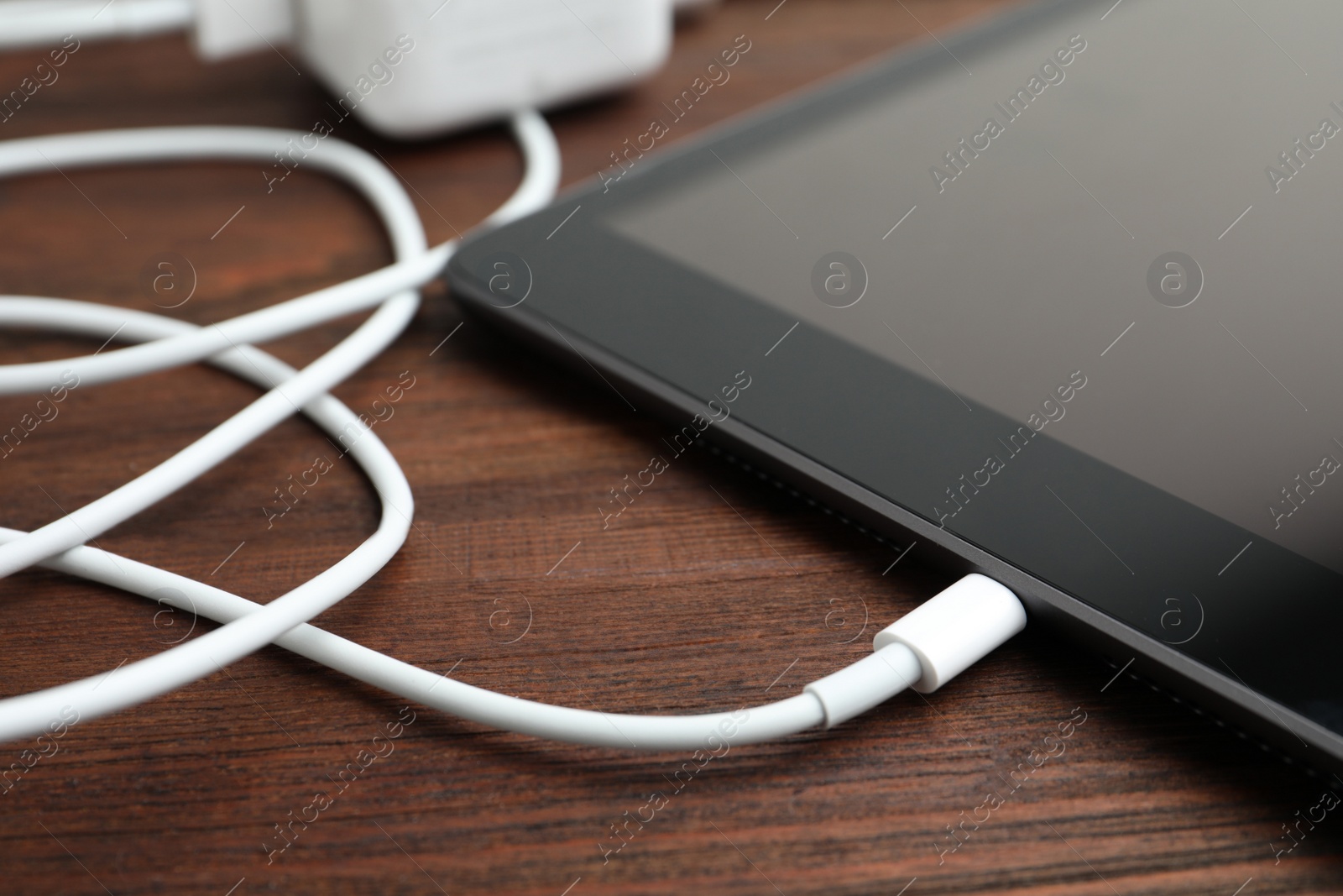 Photo of Tablet and charge cable on wooden table, closeup. Modern technology