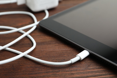 Tablet and charge cable on wooden table, closeup. Modern technology