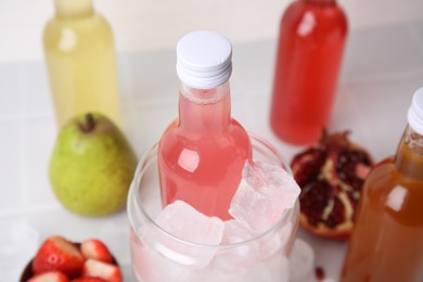 Tasty kombucha in bottles, glass with ice and fresh fruits on white table, closeup