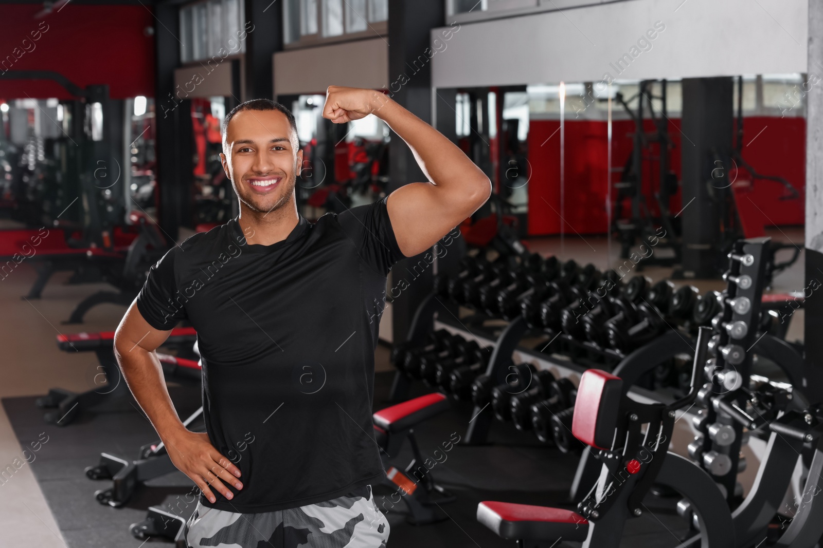 Photo of Happy trainer showing bicep in modern gym, space for text
