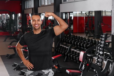 Happy trainer showing bicep in modern gym, space for text