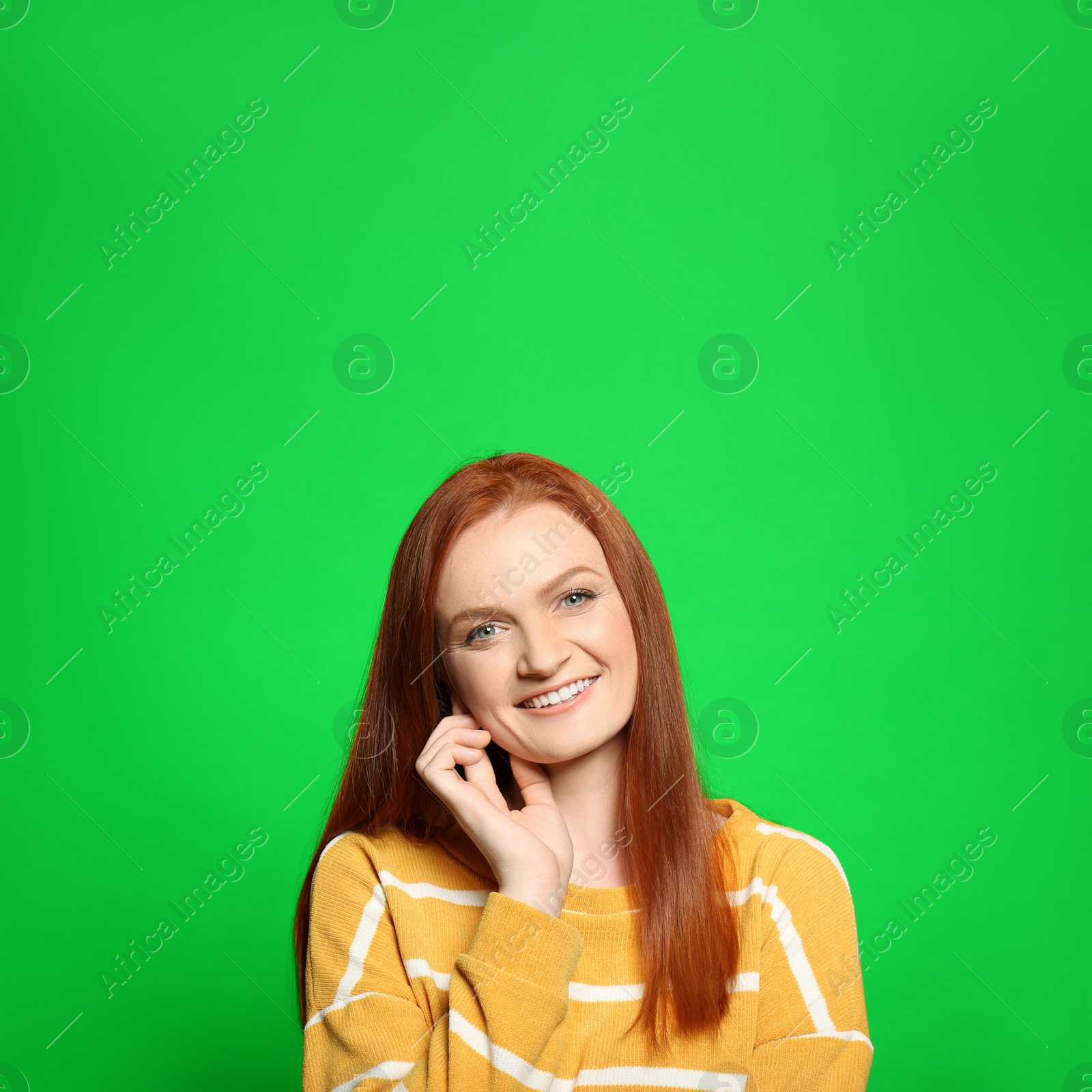 Image of Chroma key compositing. Happy young woman with red hair against green screen