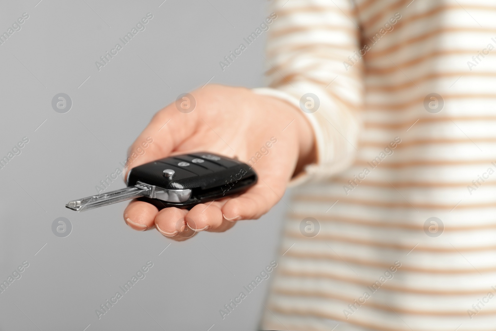 Photo of Young woman holding car key on grey background, closeup