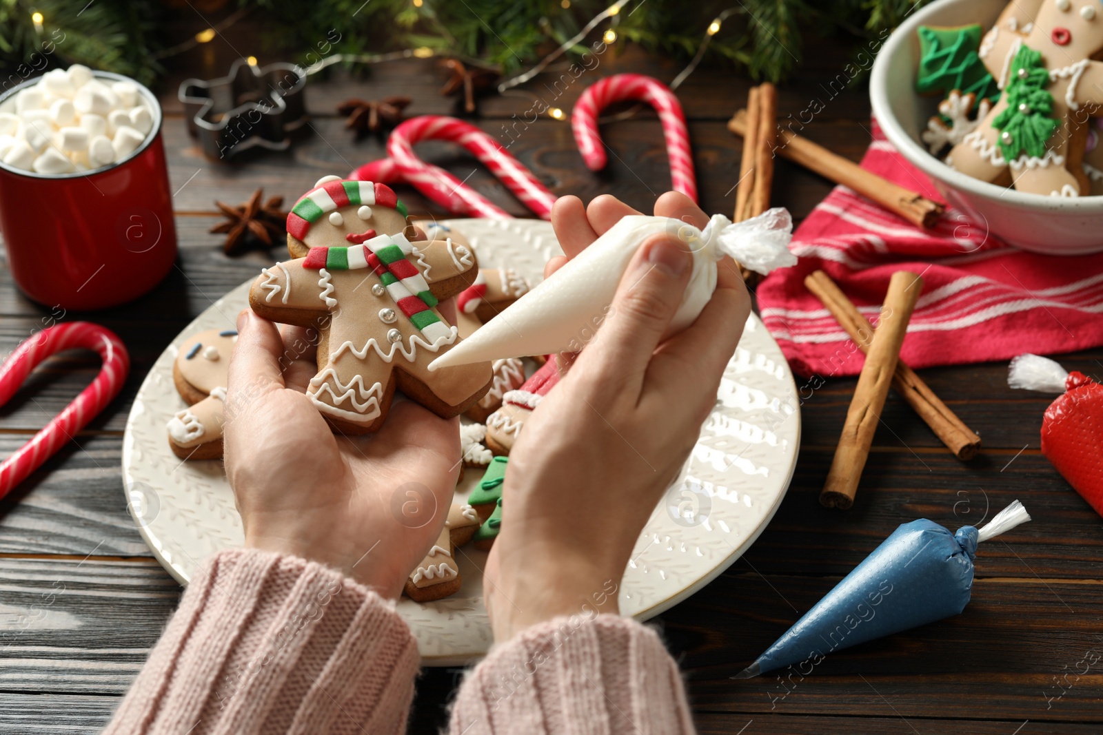 Photo of Making homemade Christmas cookies. Girl decorating gingerbread man at wooden table, closeup