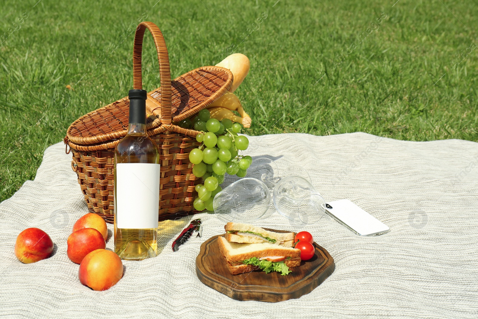 Photo of Basket with food and wineglasses on blanket prepared for picnic in park