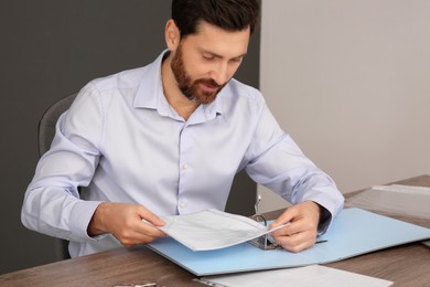 Photo of Businessman putting document into file folder at wooden table in office