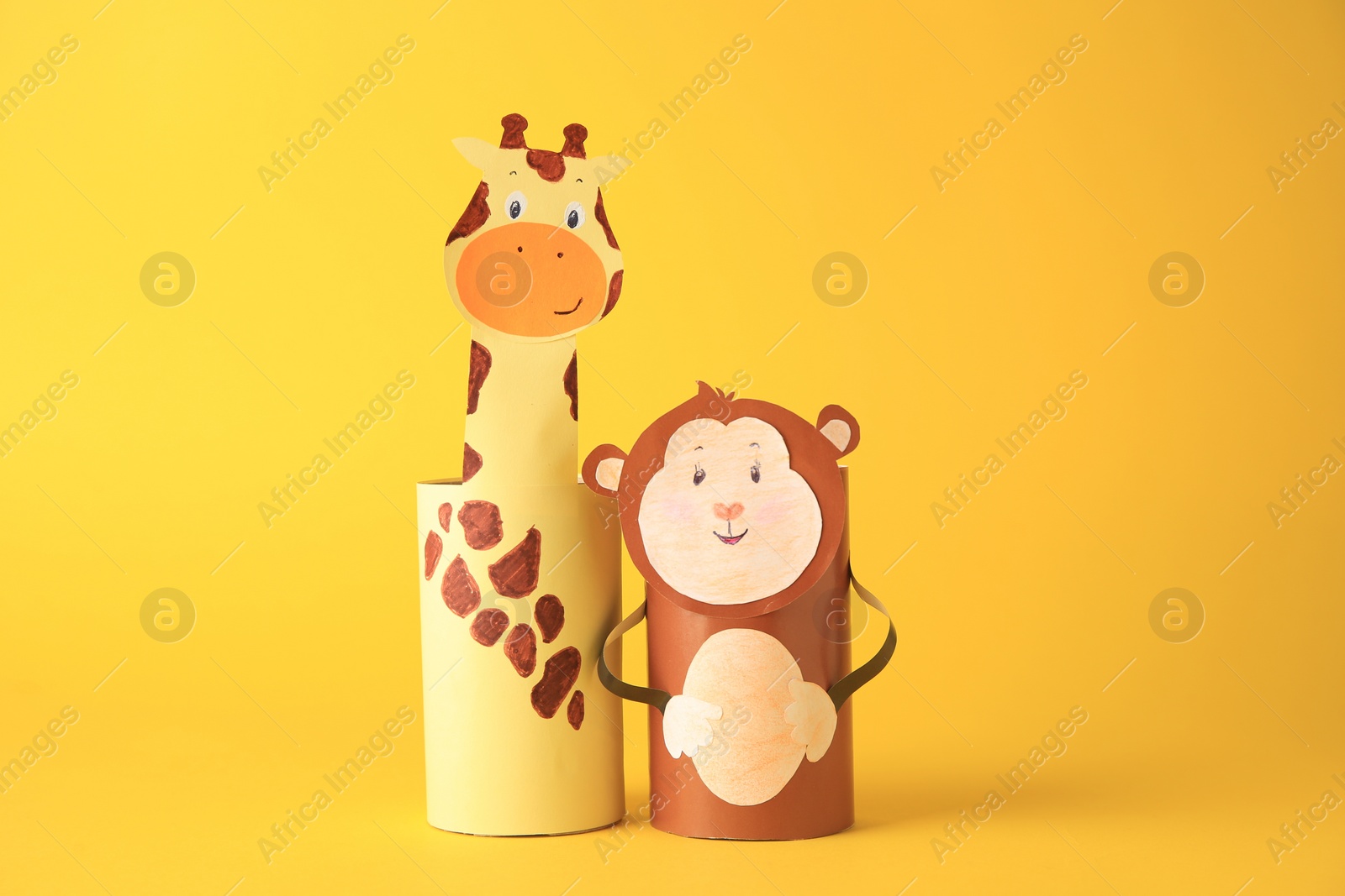 Photo of Toy monkey and giraffe made from toilet paper hubs on yellow background. Children's handmade ideas