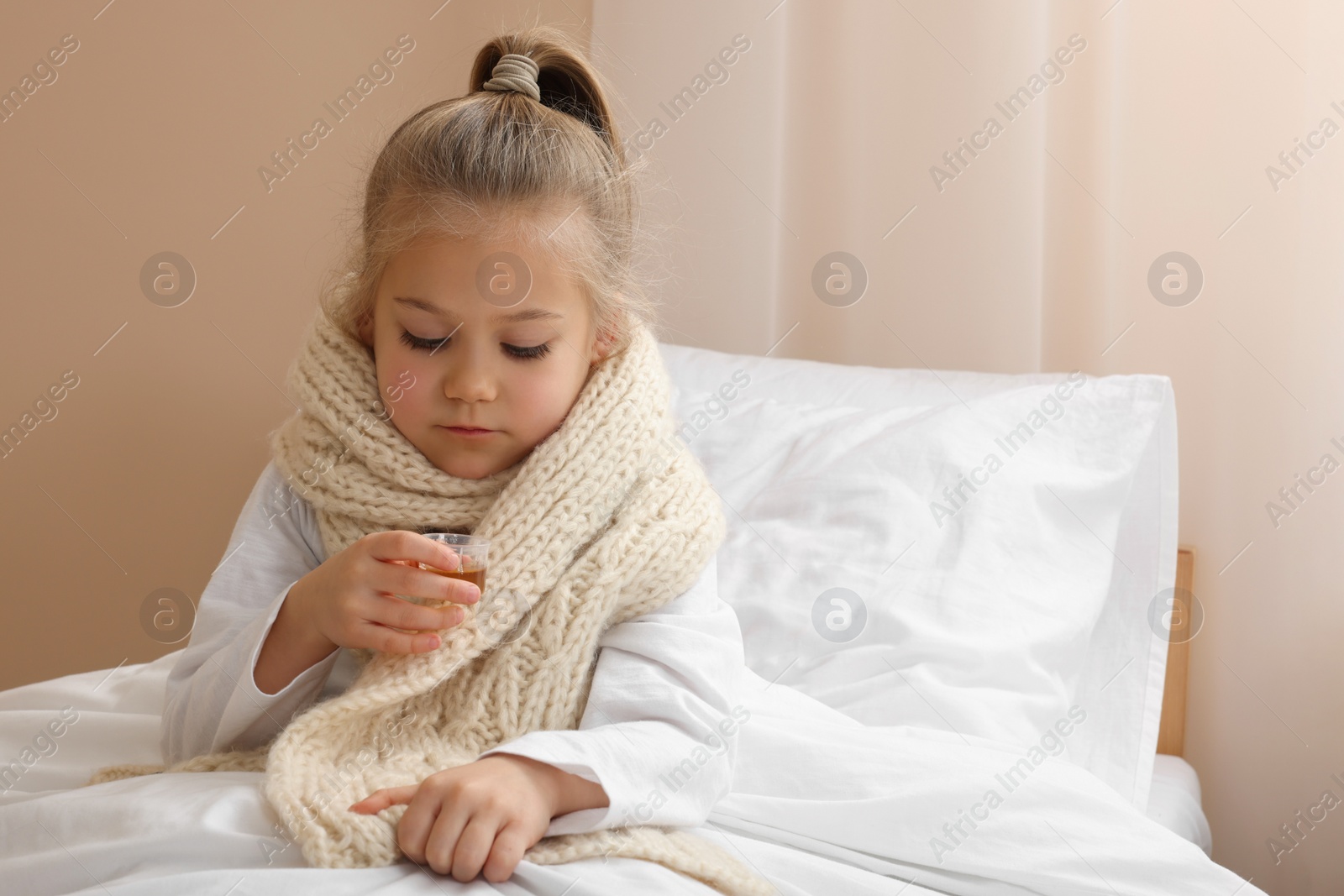 Photo of Sick girl taking cough syrup on bed at home, space for text. Cold medicine