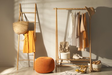 Photo of Modern dressing room interior with stylish clothes, shoes and orange pouf