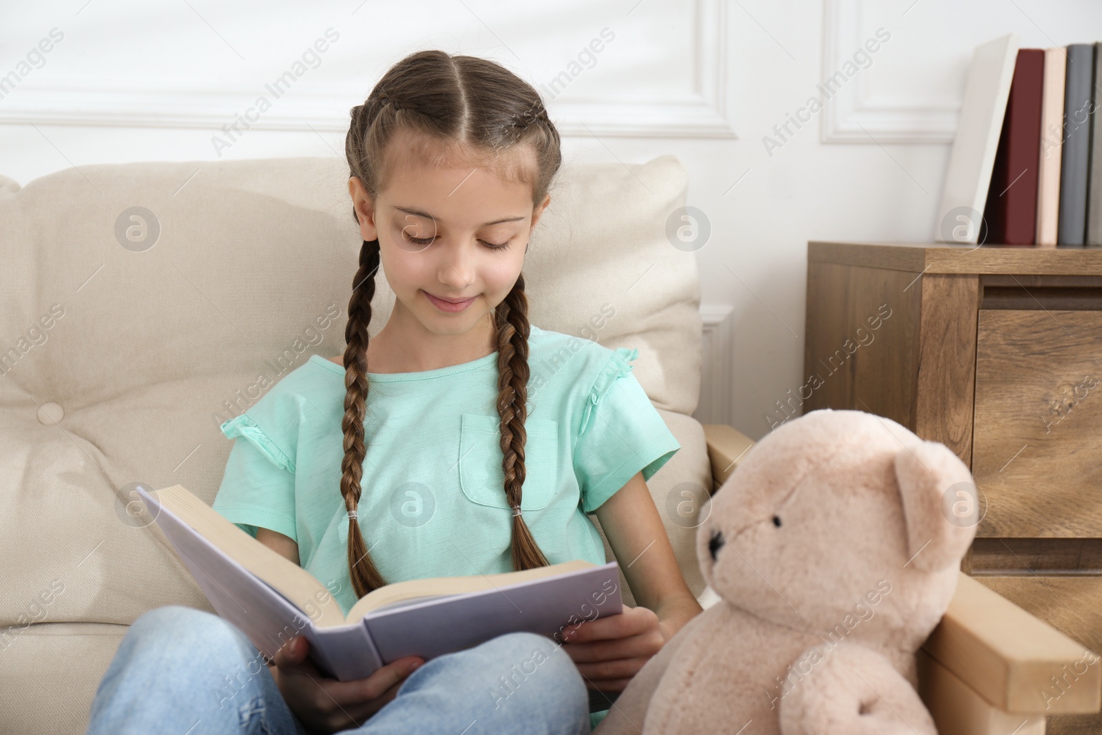 Photo of Cute little girl reading book on sofa at home