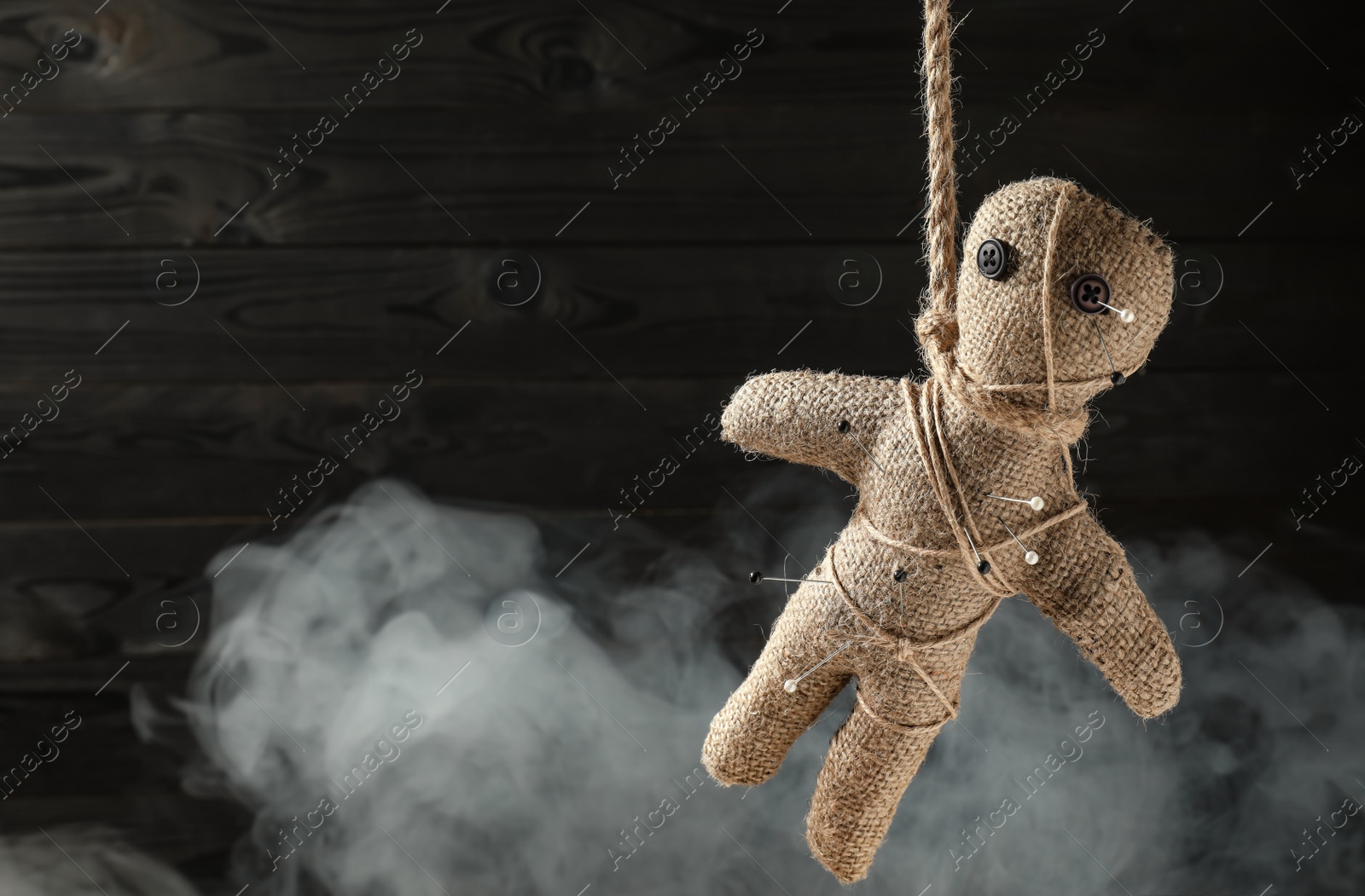 Photo of Voodoo doll with pins and smoke on dark wooden background. Space for text